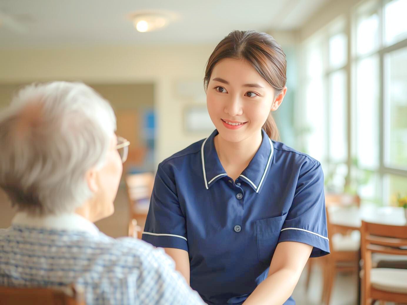 窓からの自然光の中で高齢者の肩に手を添え穏やかに微笑む介護士